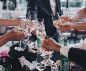 Group of people holding champagne glasses and toasting at wedding reception outdoors in the evening. Family and friends clinking glasses and cheering with alcohol at delicious feast celebration
